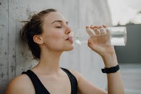Woman drinking water from glass with skincare products nearby, representing question about water and glowing skin